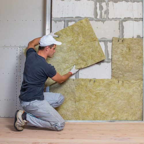 Worker insulating a room wall with mineral rock wool thermal insulation.