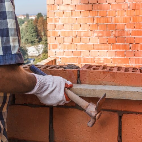 Bricklayer in protective gloves with trowel places a brick on mo